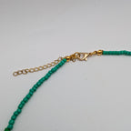 A close-up of a beaded necklace with small turquoise-green beads and gold-tone hardware, including an extender chain and lobster clasp, on a plain light background.
