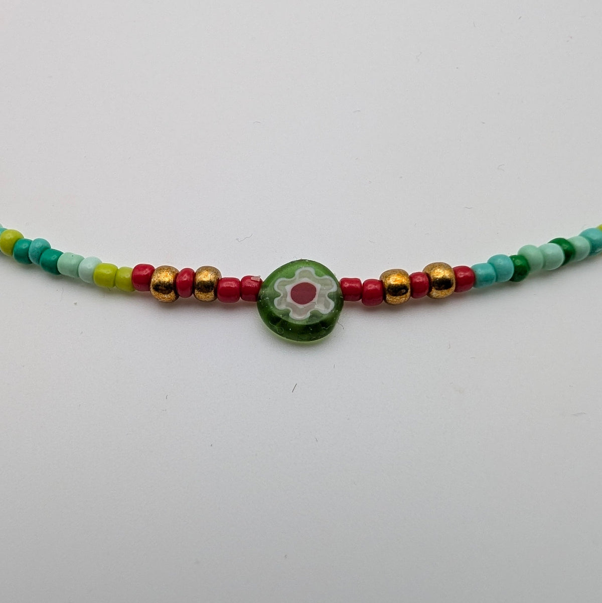 Close-up of green millefiori flower bead and gold-tone accents on multicolour choker