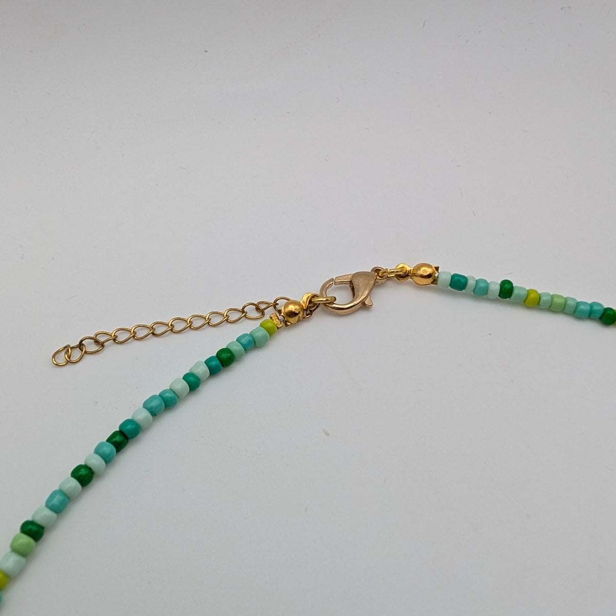 Gold-tone lobster clasp and extender chain on handmade multicolour seed bead necklace