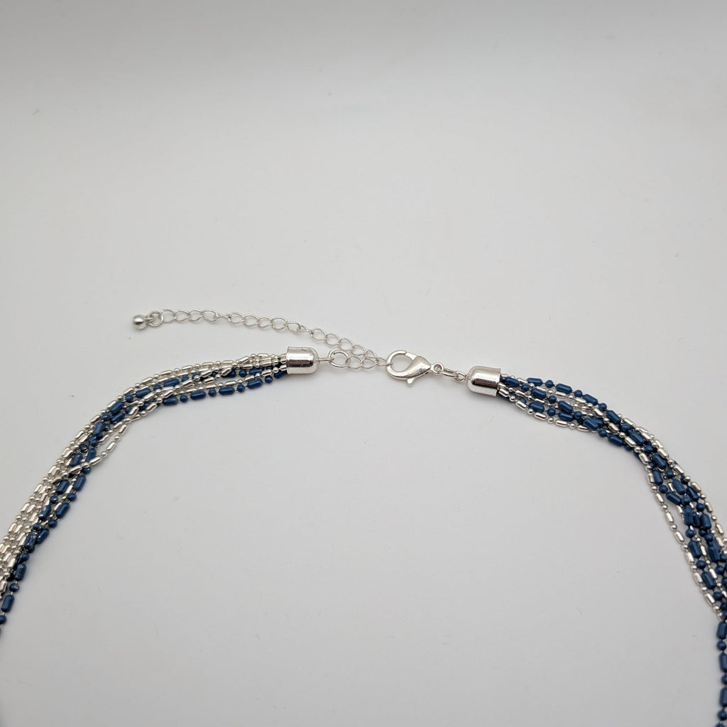 A multi-strand necklace featuring dark blue faceted beads and silver-toned chains, with a silver lobster clasp and extension chain, displayed on a light gray background.