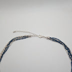 A multi-strand necklace featuring dark blue faceted beads and silver-toned chains, with a silver lobster clasp and extension chain, displayed on a light gray background.