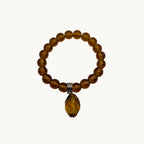 A beaded stretch bracelet made of translucent amber-brown beads with a faceted amber coloured teardrop pendant and a small silver tone spacer, shown on a plain light background.