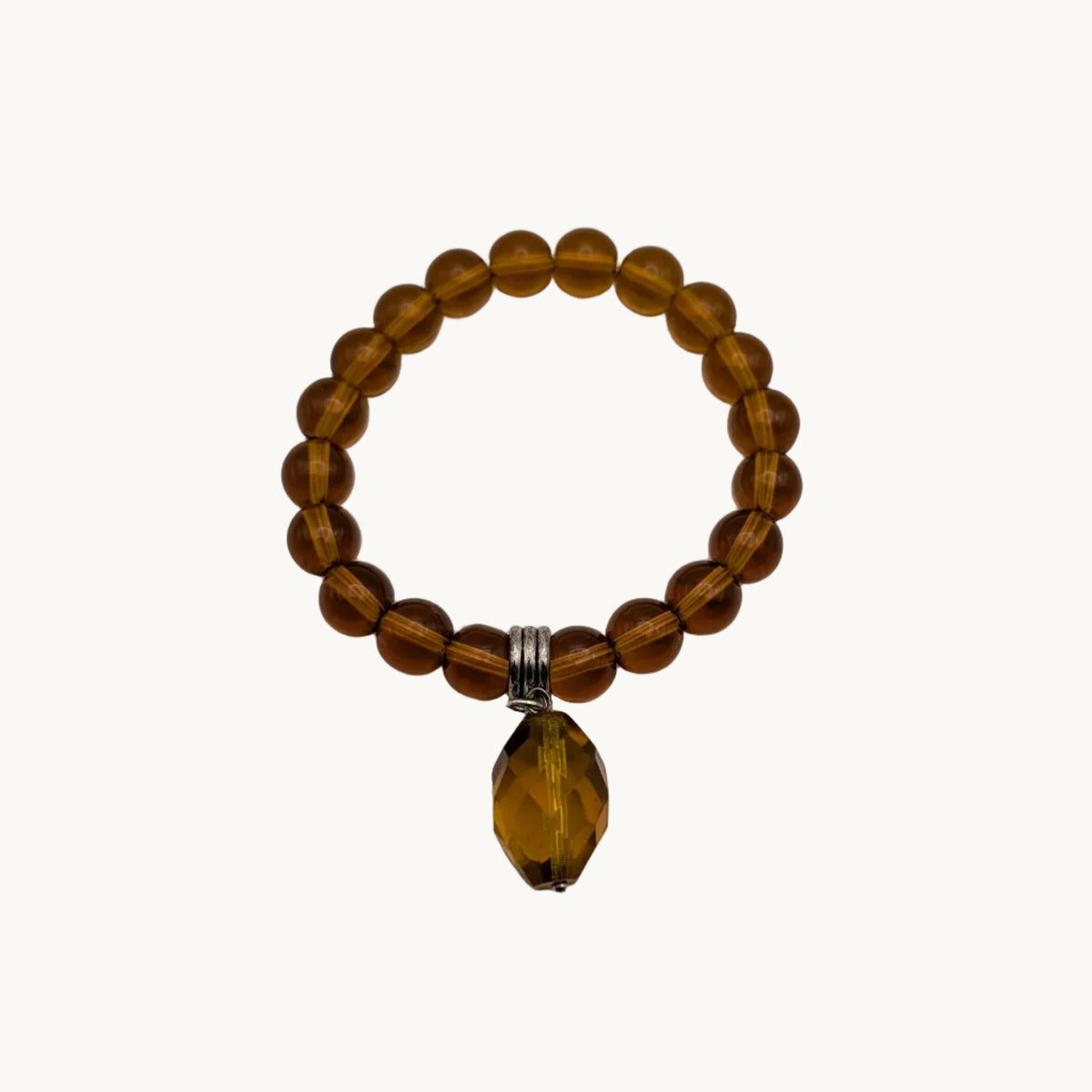 A beaded stretch bracelet made of translucent amber-brown beads with a faceted amber coloured teardrop pendant and a small silver tone spacer, shown on a plain light background.