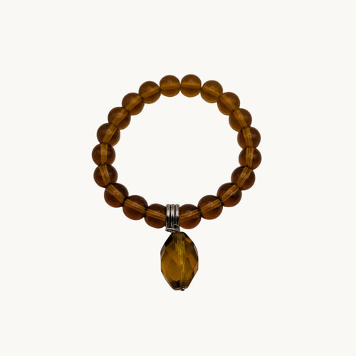 A beaded stretch bracelet made of translucent amber-brown beads with a faceted amber coloured teardrop pendant and a small silver tone spacer, shown on a plain light background.