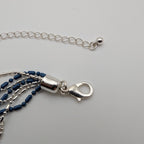 Close-up of a silver chain necklace with a lobster clasp and layered dark blue beaded strands, photographed on a light gray background.
