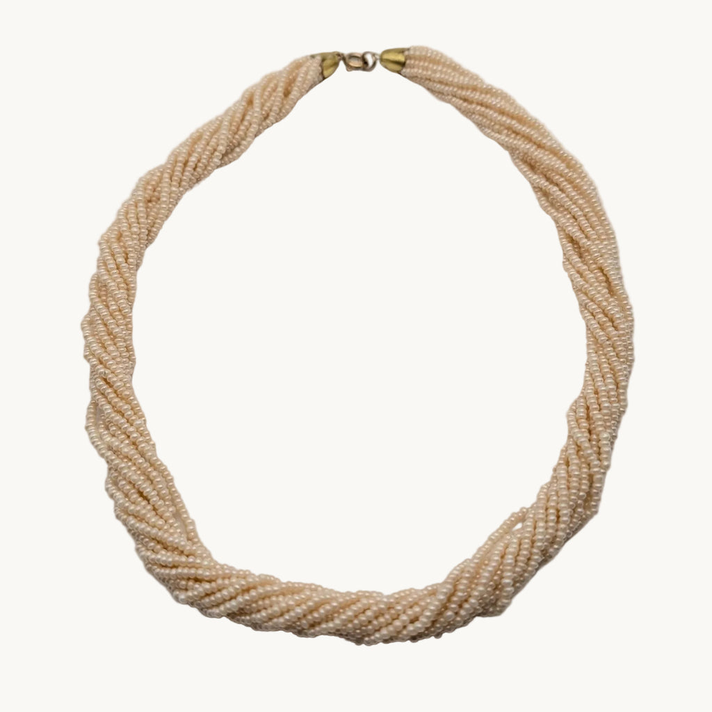 A multi-strand twisted rope necklace made of small cream-colored beads, featuring a gold clasp at the top, displayed on a neutral light gray background.