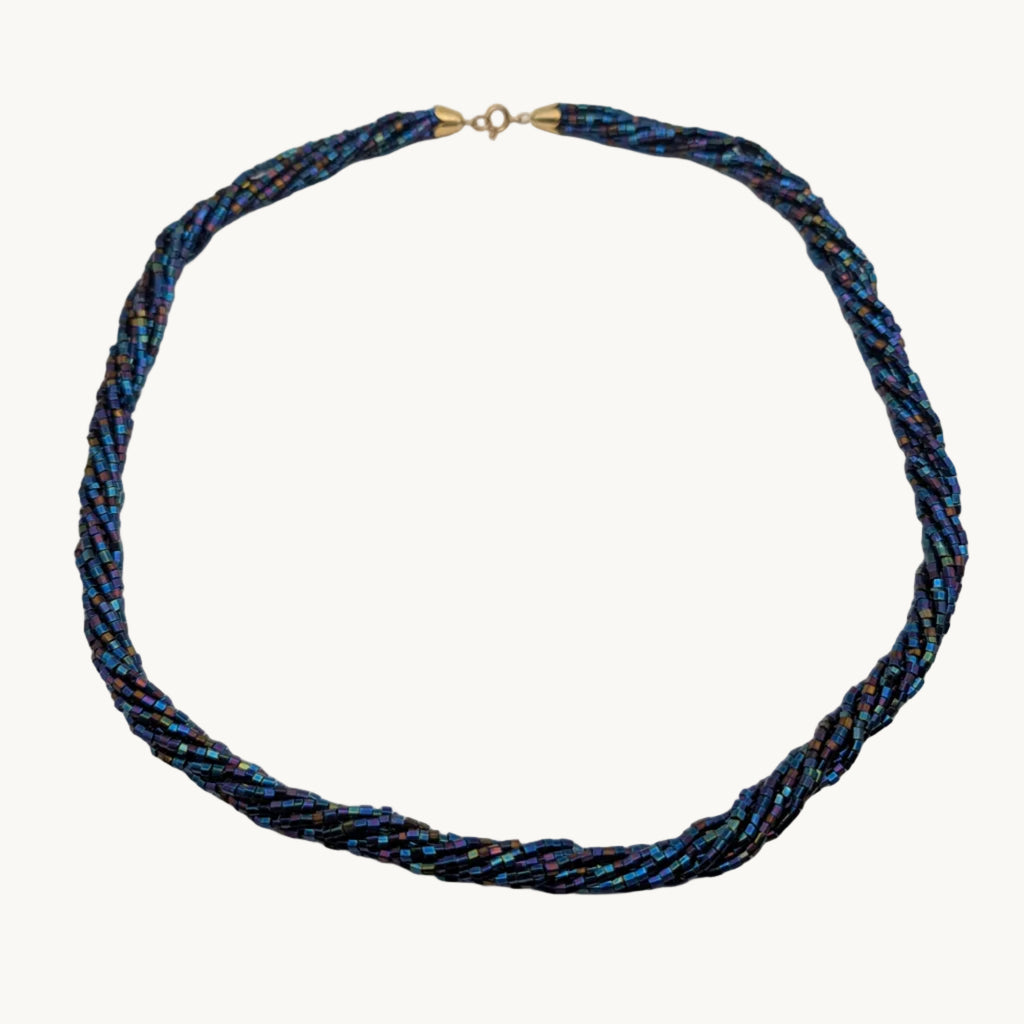A twisted braided necklace made of blue, black, and gold metallic threads, featuring a small gold clasp at the top, displayed on a plain light gray background.