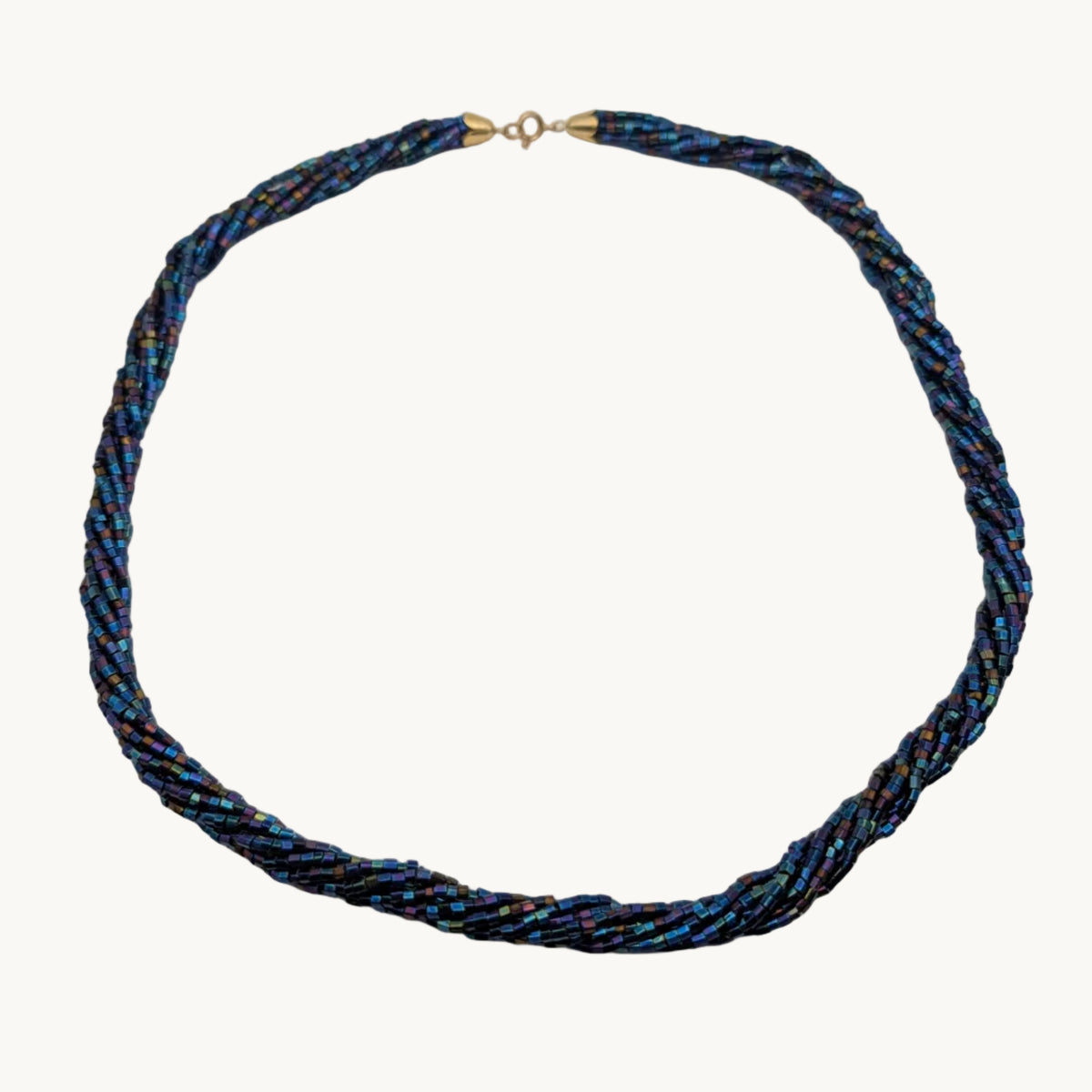 A twisted braided necklace made of blue, black, and gold metallic threads, featuring a small gold clasp at the top, displayed on a plain light gray background.