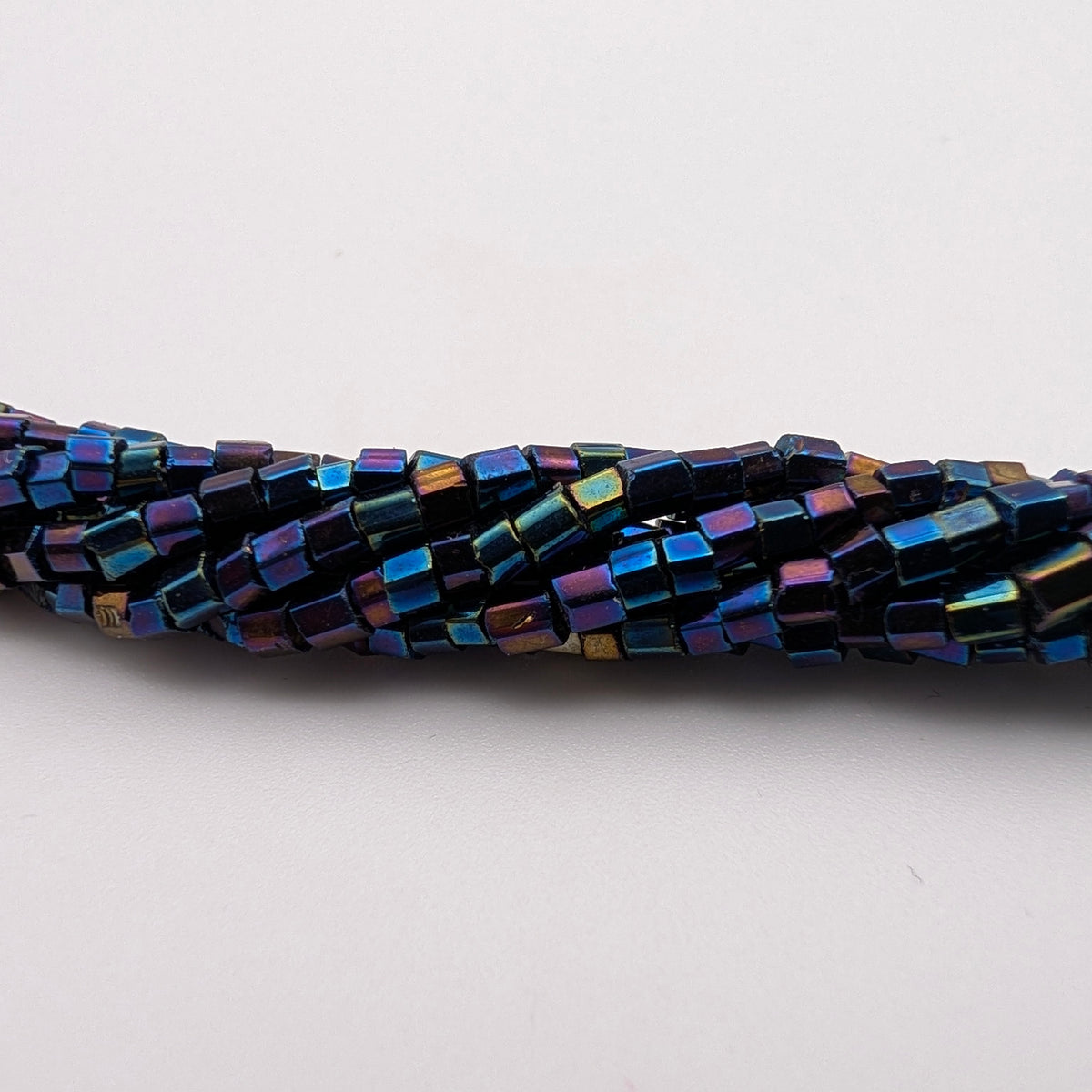 A close-up of a strand of small rectangular iridescent beads on a plain white background.
