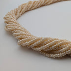 A close-up of a multi-strand pearl necklace arranged in a twisted knot on a plain white background.