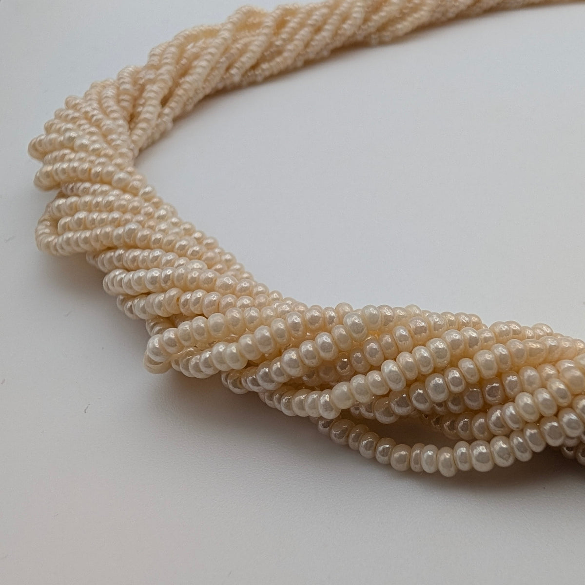 A close-up of a multi-strand pearl necklace arranged in a twisted knot on a plain white background.
