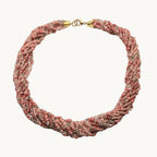 A multi-strand beaded wrap choker necklace in a dusty rose pink and beige colorway, featuring gold-toned metal clasp details, displayed on a neutral light gray background.