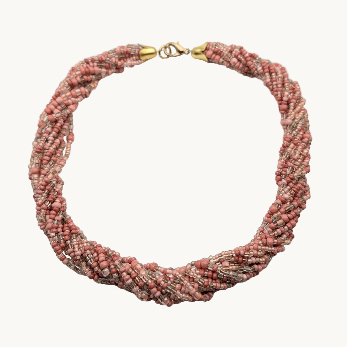 A multi-strand beaded wrap choker necklace in a dusty rose pink and beige colorway, featuring gold-toned metal clasp details, displayed on a neutral light gray background.