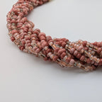 A close-up of a multi-strand beaded necklace made of round dusty pink beads and clear faceted beads, arranged on a plain light background.
