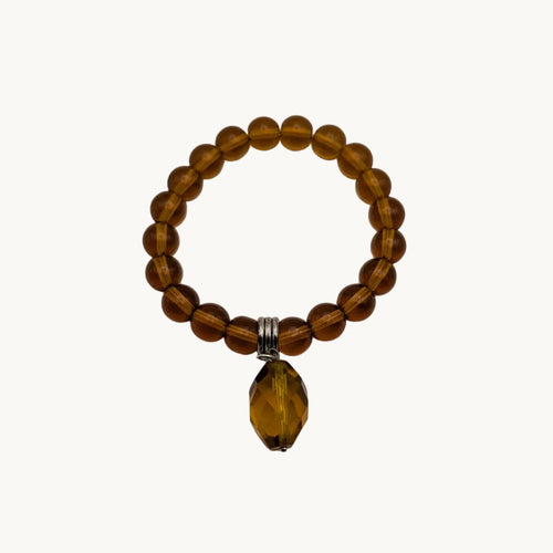 A beaded stretch bracelet made of translucent amber-brown beads with a faceted amber coloured teardrop pendant and a small silver tone spacer, shown on a plain light background.